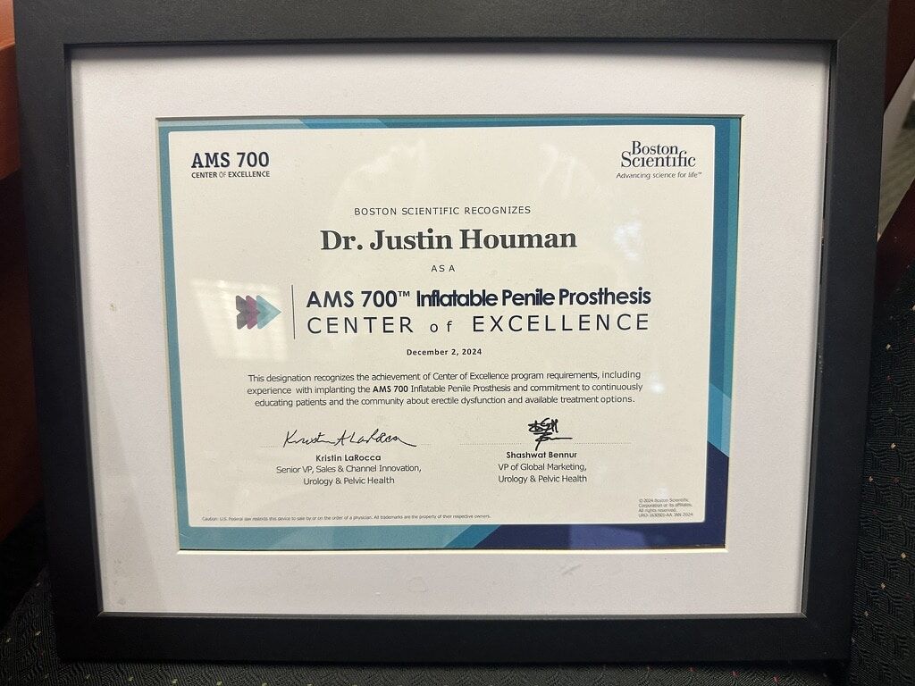 A close-up of a framed certificate, dated December 2, 2024, from Boston Scientific, designating Dr. Justin Houman as an AMS 700™ Inflatable Penile Prosthesis Center of Excellence for his experience and commitment.